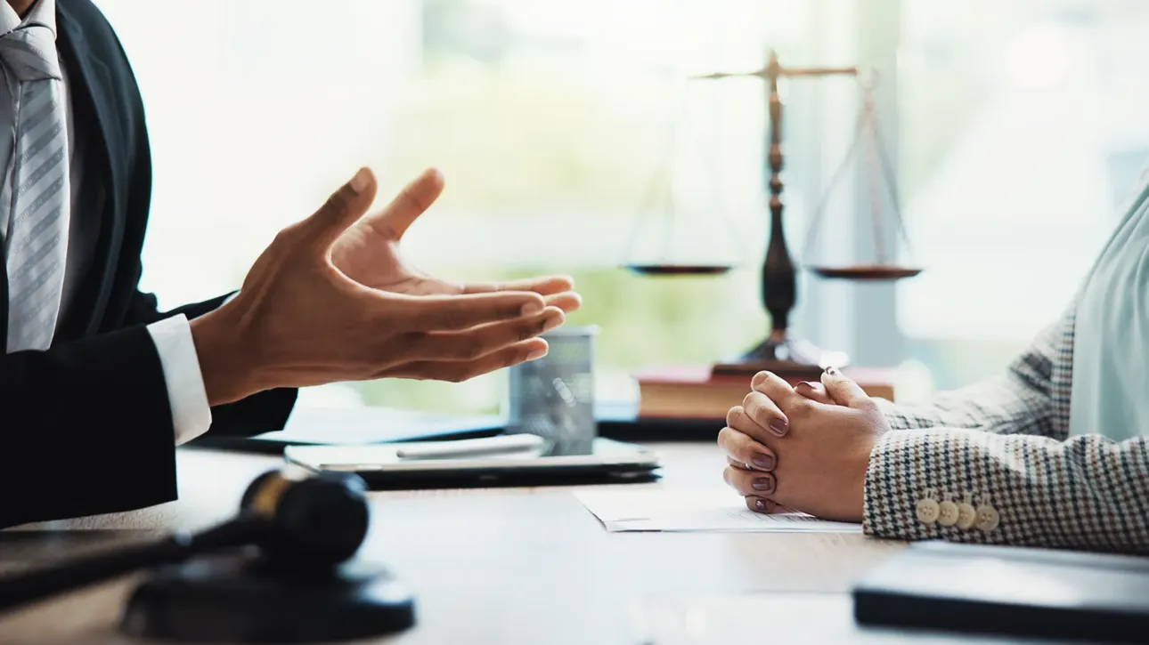 Abogado y cliente en una reunión de mediación legal con balanza de la justicia en el fondo.
