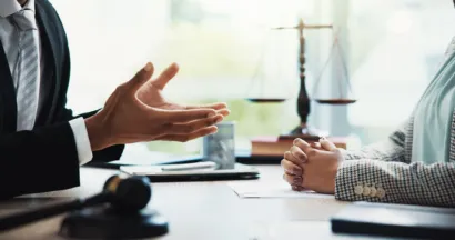 Abogado y cliente en una reunión de mediación legal con balanza de la justicia en el fondo.