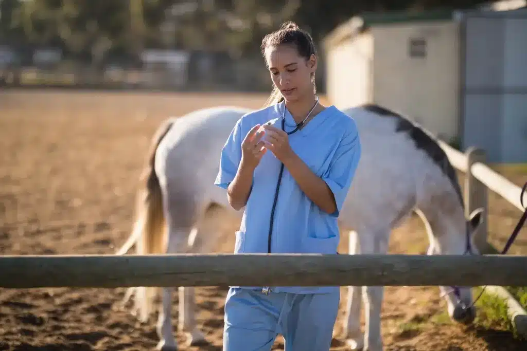Veterinaria preparando una inyección en un entorno rural con un caballo de fondo.